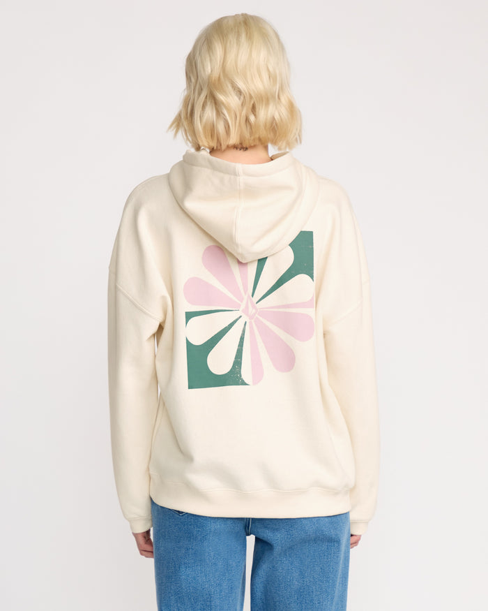 A woman with short blond hair models the Volcom Women's Stone Art Up Hoodie—an oversized, cream fleece with a pink and green abstract floral back design—paired with blue jeans. Shown from behind against a plain background for a cozy streetwear look.
