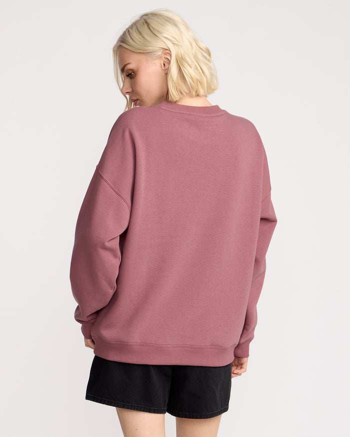 A woman with short blonde hair wears the Volcom Women's Stone Crew and black shorts, standing with her back to the camera and head turned left against a plain light background.
