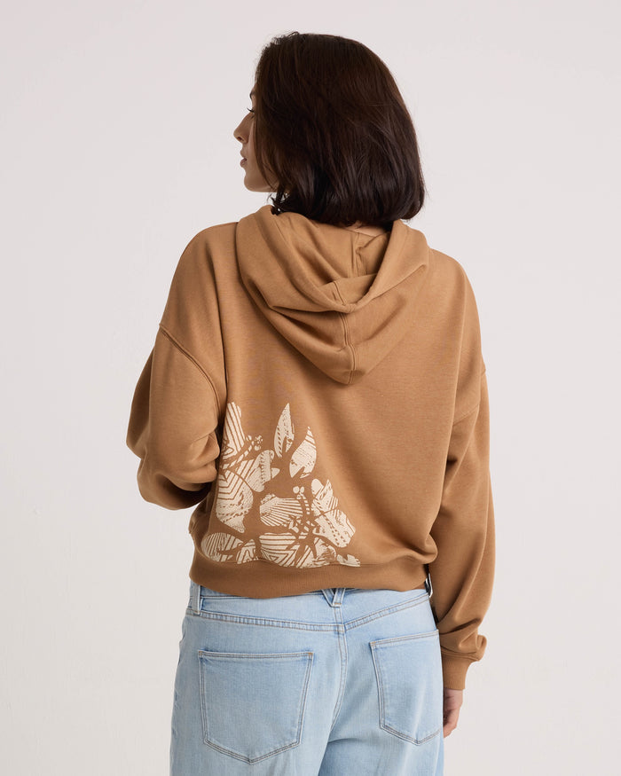 A person with shoulder-length dark hair, dressed in a relaxed-fit Volcom Women's Stone Dream Hoodie with a white geometric animal graphic on the back and light blue jeans, stands facing away from the camera.