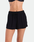 A person is wearing Volcom's Women's Stone Shine Short Vsc in black with an elastic waistband and a black bra, revealing a butterfly tattoo on their ribcage; the photo is cropped from upper chest to mid-thigh against a plain background.