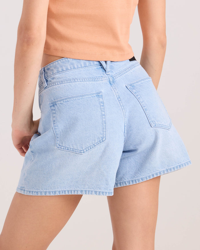 A person is shown from the back wearing Volcom Women's Stoned Bf Short in a light wash with visible back pockets, paired with a peach top. The shorts feature a 5-inch inseam and boyfriend fit style.