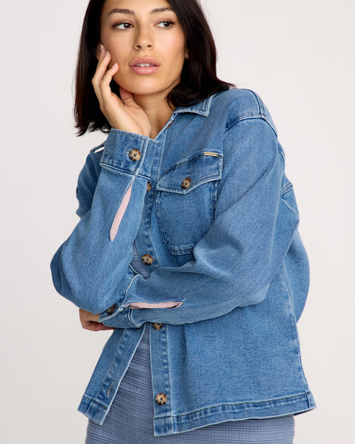 A woman with straight dark hair wears the Volcom Women's Stoned BF Shacket over a ribbed gray top, gazing to the side with her hand on her cheek against a simple, light-colored background.