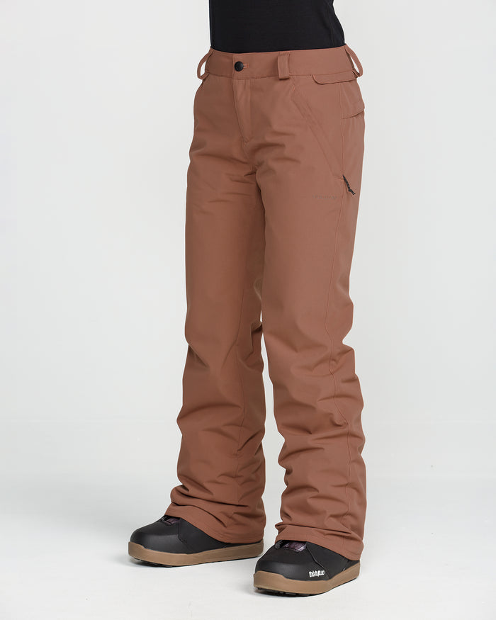 A person is wearing Volcom Women’s Stoned Insulated Pants in brown and black boots, standing against a plain white background. The image focuses on the lower body to highlight the pants’ 10K waterproof rating and recycled insulation, with nothing visible above the waist.