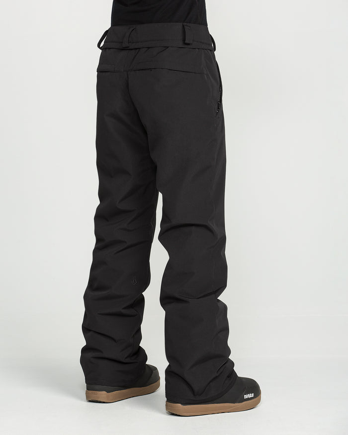 A person wearing loose-fitting black Volcom Women’s Stoned Insulated Pants and black snow boots stands on a white background with their back facing the camera.