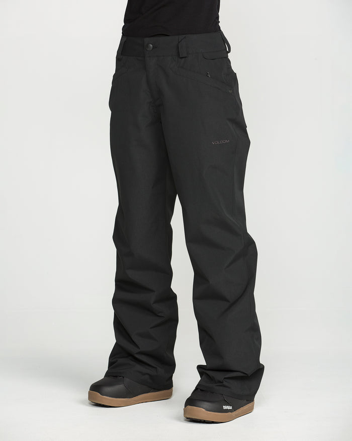 A person wearing black Volcom Women’s Stoned Pants and black boots with brown soles stands against a plain white background, with only the lower half of the body visible.