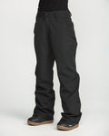 A person wearing black Volcom Women’s Stoned Pants and black boots with brown soles stands against a plain white background, with only the lower half of the body visible.