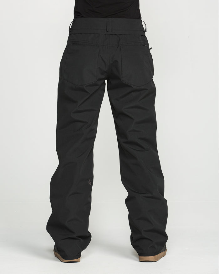 A person wearing Volcom Women’s Stoned Pants—loose-fitting black pants with a V-Science 2-Layer construction for waterproof performance—paired with brown shoes, stands against a plain white background. Only the person’s lower back and legs are visible; the upper body is not shown. These stylish yet practical women’s pants are designed for comfort and protection.