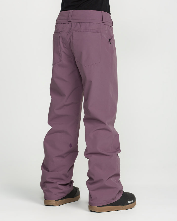 A person is shown from the back against a plain white background, wearing loose-fitting purple Volcom Women’s Stoned Pants and black shoes.