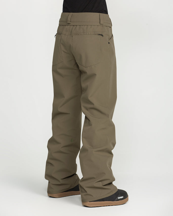 A person is shown from behind against a plain white background, wearing Volcom Women’s Stoned Pants in a khaki color and black boots. These slim, mid-rise waterproof ski pants feature back pockets and reinforced seams.