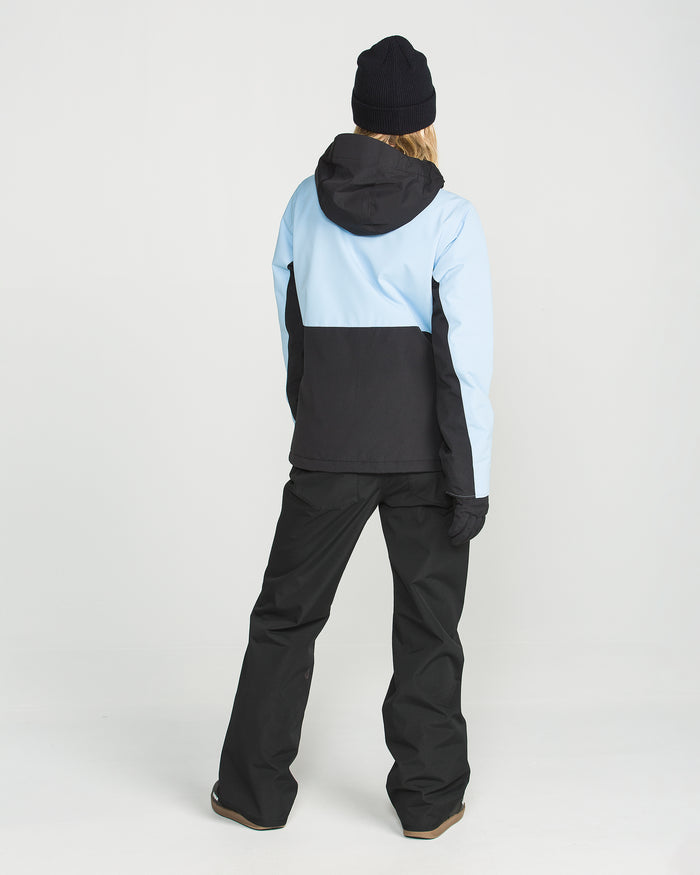 A person wearing a light blue and black jacket, black gloves, a black beanie, and the Volcom Women’s Stoned Pants in slim mid-rise with V-Science 2-Layer waterproof technology stands facing away from the camera against a plain white background.