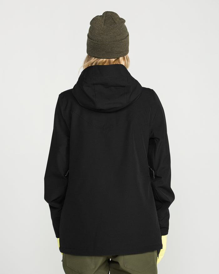 A person wearing the Volcom Women’s Stoney Shadow Insulated Jacket, an olive green knit beanie, olive green pants, and yellow gloves stands facing away from the camera against a plain white background.