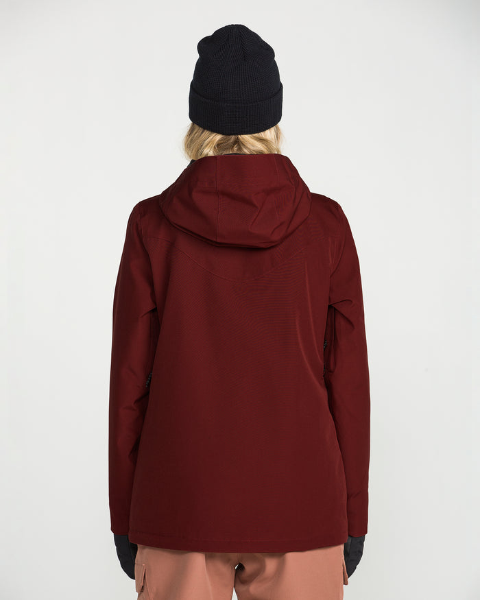 A person wearing the Volcom Women’s Stoney Shadow Insulated Jacket in maroon, styled with a black beanie and pink pants, stands facing away from the camera against a plain white background.