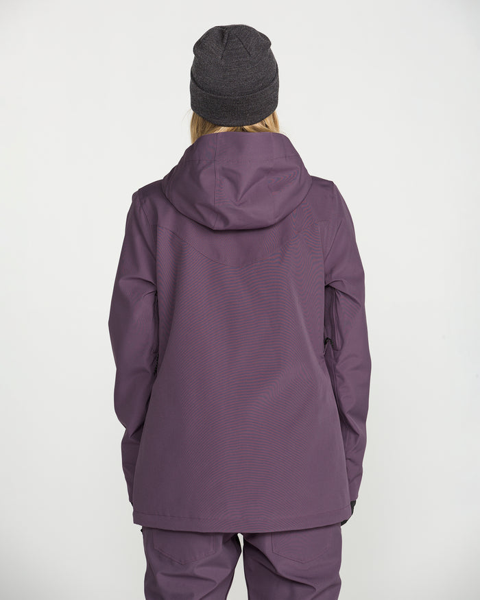 A person wearing the Volcom Women’s Stoney Shadow Insulated Jacket in purple, paired with matching pants and a dark beanie, stands facing away from the camera against a plain white background.