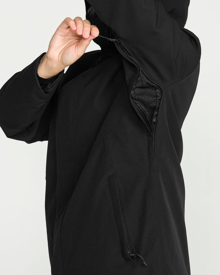 A woman wearing the Volcom Women’s Stoney Shadow Insulated Jacket in black lifts her arm to reveal an underarm zipper vent, showing the jacket’s breathable mesh lining.
