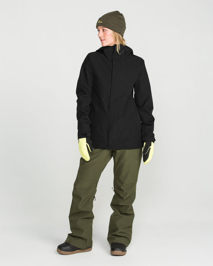 Wearing the Volcom Women’s Stoney Shadow Insulated Jacket, along with olive green pants, yellow gloves, black boots, and an olive beanie, a person stands facing slightly to the side against a plain light background.