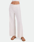 A person is shown from the waist down against a plain white background wearing Volcom Women's Sun Lounge Pants in white, featuring a high-waisted, wide-leg ribbed design with an elastic waistband, paired with tan sandals.