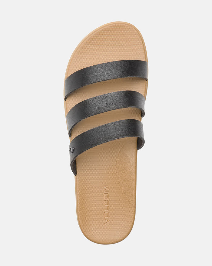 A tan Women’s Sunseeker Sandal by Volcom with three black horizontal straps and a flat sole, viewed from above. The Volcom logo is embossed on the footbed.