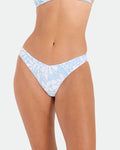 A woman models the Volcom Women's Tribal Stone 90S V Bottom, a skimpy, high-cut bikini made from recycled nylon in a light blue and white print. Only her torso and upper thighs are shown against a plain white background.