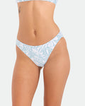 A woman models Volcom's Women's Tribal Stone Hipster Full Bikini Bottom in Summer Song, made from recycled nylon; she stands against a plain white background, showing her midsection, upper thighs, and a small tattoo near her waist.
