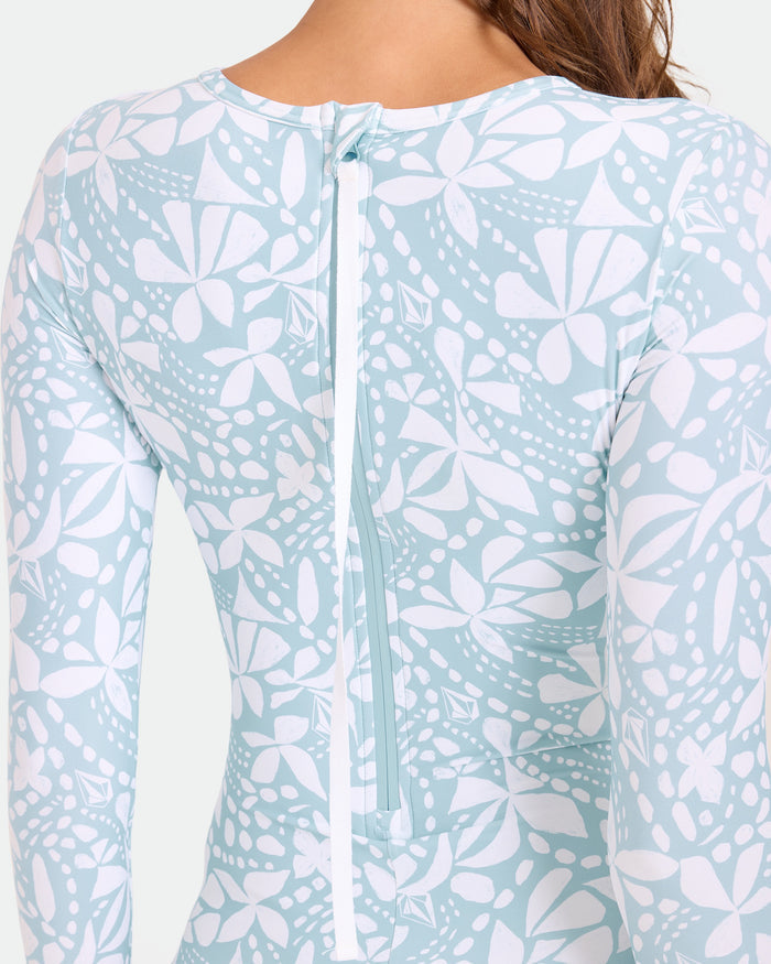 A close-up of a person wearing the Volcom Women's Tribal Stone Surf Suit, featuring light blue and white abstract floral print, long sleeves, cheeky coverage, and a visible white back zipper.