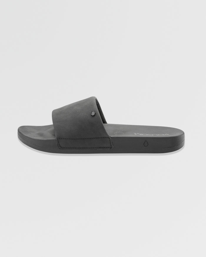The Women's Volcation Slides by Volcom are black slide sandals featuring a wide single strap and flat sole for everyday comfort, ideal for summer wear. Shown against a white background.