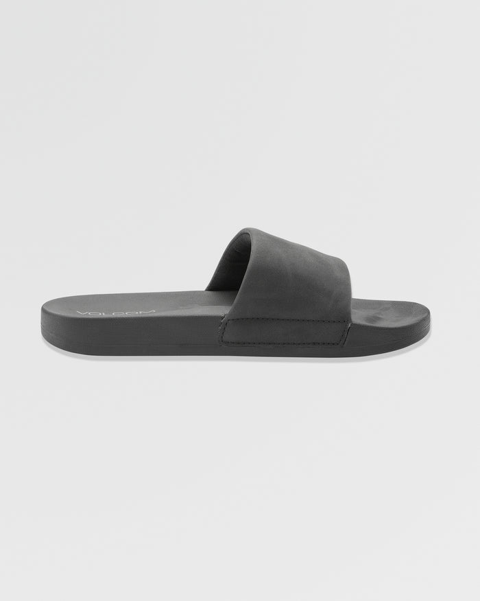 The Women's Volcation Slides by Volcom are black summer sandals with a wide single strap and flat sole, delivering everyday comfort and signature style. Shown in side profile on a plain white background.