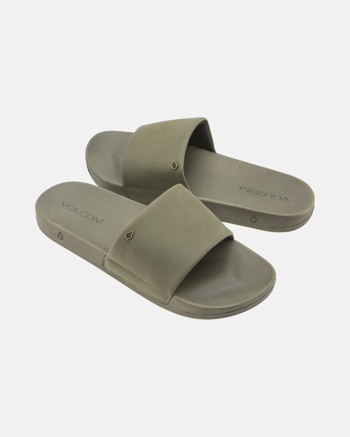 The Women's Volcom Volcation Slides feature olive green wide straps and flat soles, offering everyday comfort and classic Volcom style, shown against a white background.