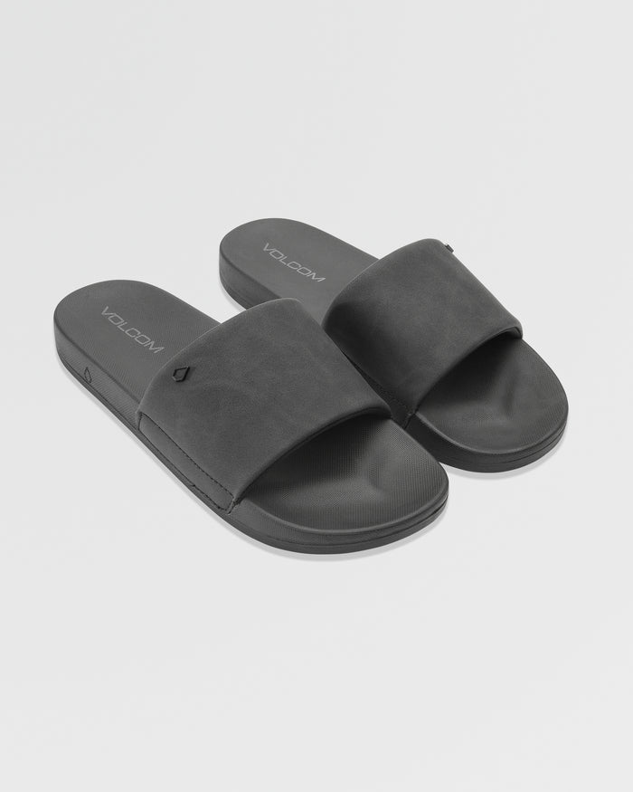 Women's Volcom Volcation Slides feature wide black straps and flat soles, angled on a plain white background. The insoles display the Volcom logo, highlighting signature style and comfort for everyday summer wear.
