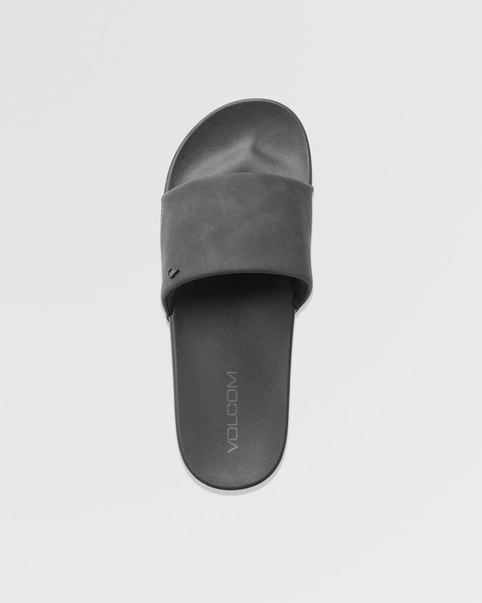 A single black Women's Volcation Slide by Volcom, featuring a wide strap and flat sole, is shown from above on a plain white background. The footbed displays the Volcom logo, highlighting its everyday comfort design.