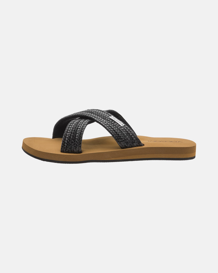 The Volcom Women's Double Cross Sandals feature a brown flat sole and black textured crisscross straps, shown from the side against a plain white background.