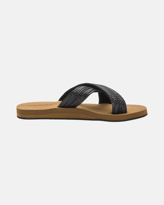 The Women's Volcom Double Cross Sandal by Volcom features a tan sole and two black textured crisscross straps, displayed from the side against a plain white background.