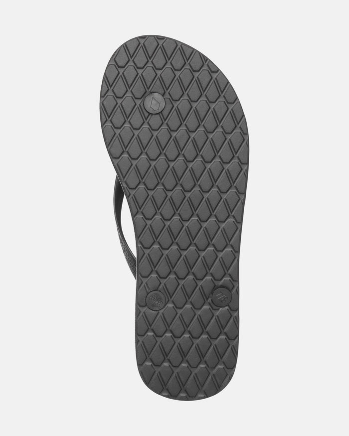The image shows the sole of the Volcom Women's Volcomotion sandal in black, featuring a diamond-patterned tread and two round plugs on the underside, showcasing classic Volcom style for everyday comfort.