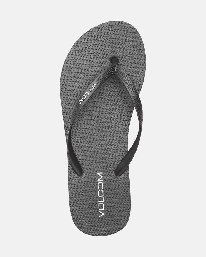 The Volcom Women's Volcomotion flip-flop features a gray textured sole, black straps, and white Volcom branding on the footbed and strap—combining everyday comfort with signature style against a clean white background.
