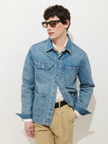 A man in dark sunglasses and the Work Jacket in Vintage Wash Denim over a white shirt with relaxed beige pants stands against a white background, one hand in his pocket, channeling an effortless Alex Mill vibe.